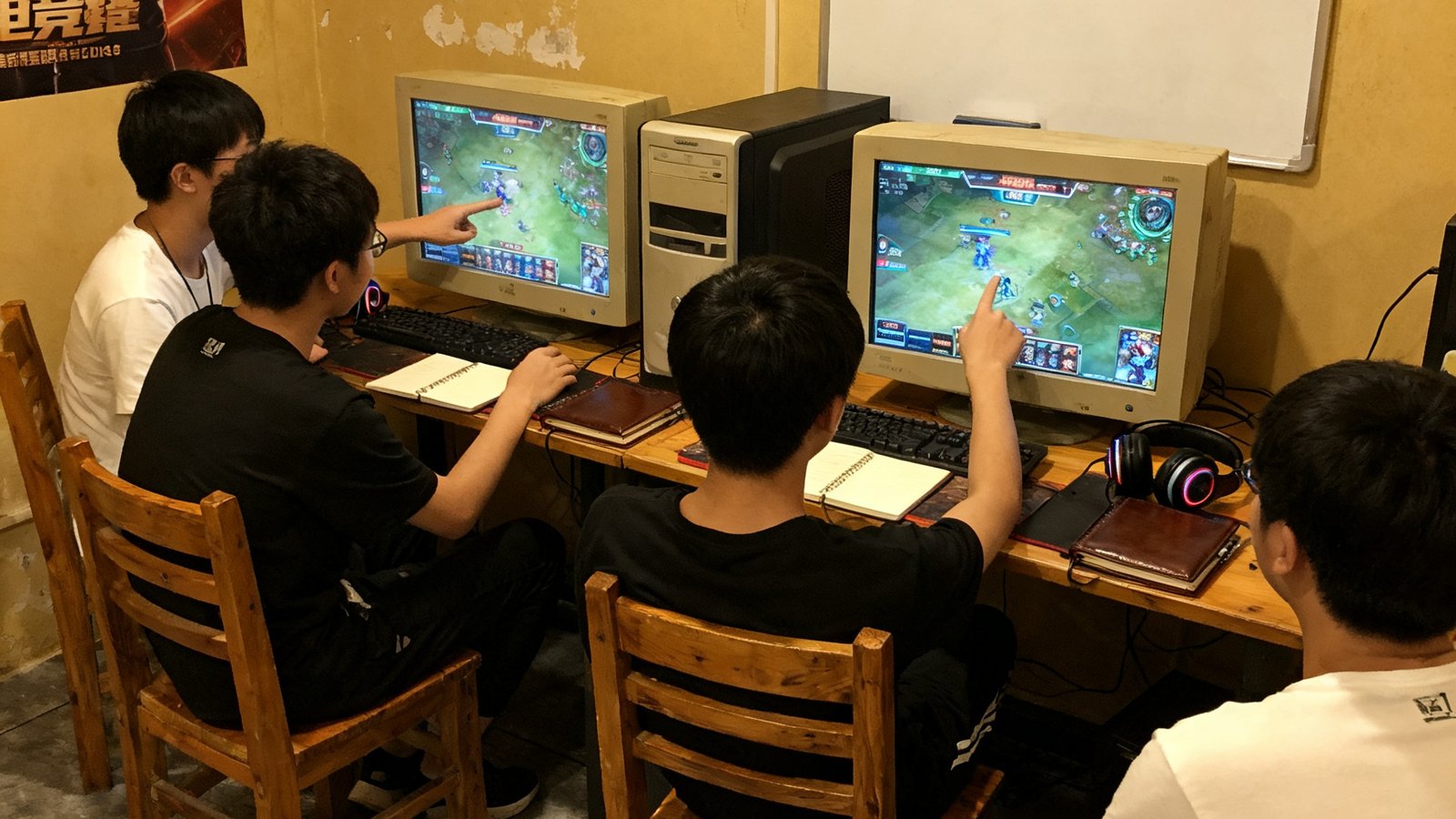 2018年的电竞训练室，几名选手围坐在台式电脑前讨论战术，白板上手写着英雄BP策略，桌上散落着笔记本和耳机，环境简朴但充满热情。